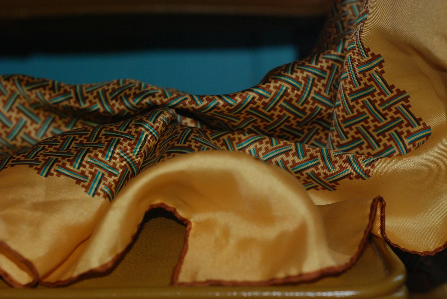 Geometric patterned silk scarf with gold border drapes elegantly.