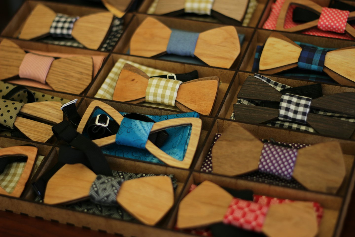 Handcrafted wooden bow ties displayed in partitioned wooden boxes.