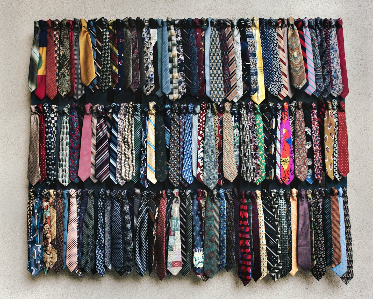 Many colorful neckties hang in neat rows on a display.