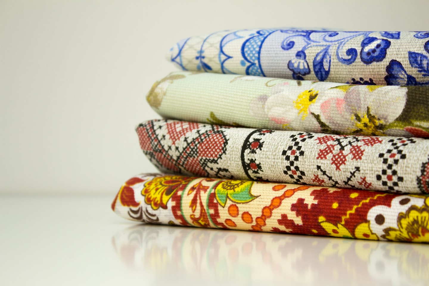 Stack of four folded patterned textiles on a white surface.